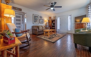A living room with a wooden floor, a ceiling fan, a sofa, a coffee table, and a lamp.