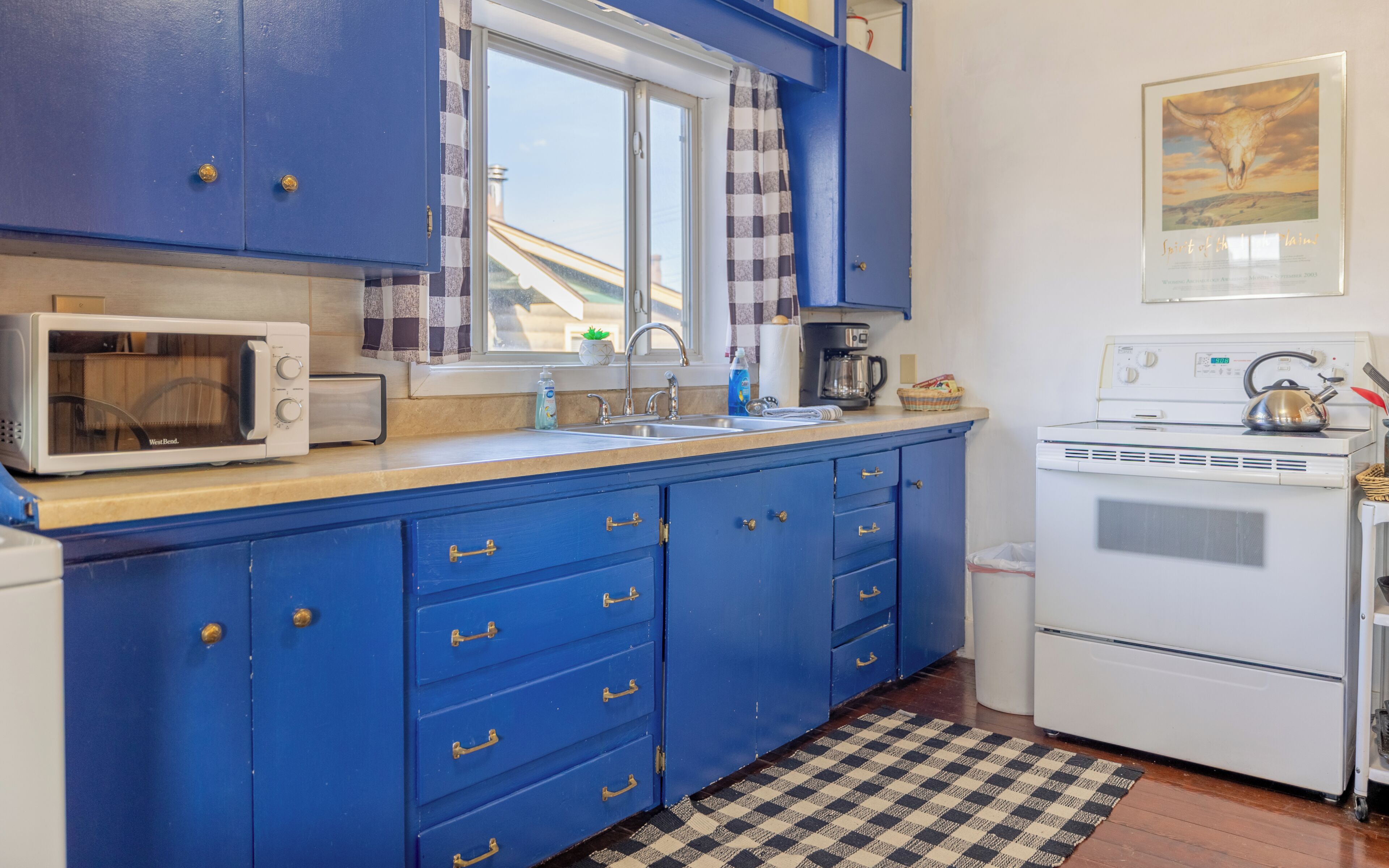 A kitchen with blue cabinets, a microwave, a kettle, and a stove.