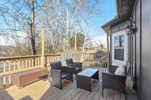 A wooden deck with wicker furniture, a barbecue grill, and a view of trees and a house.