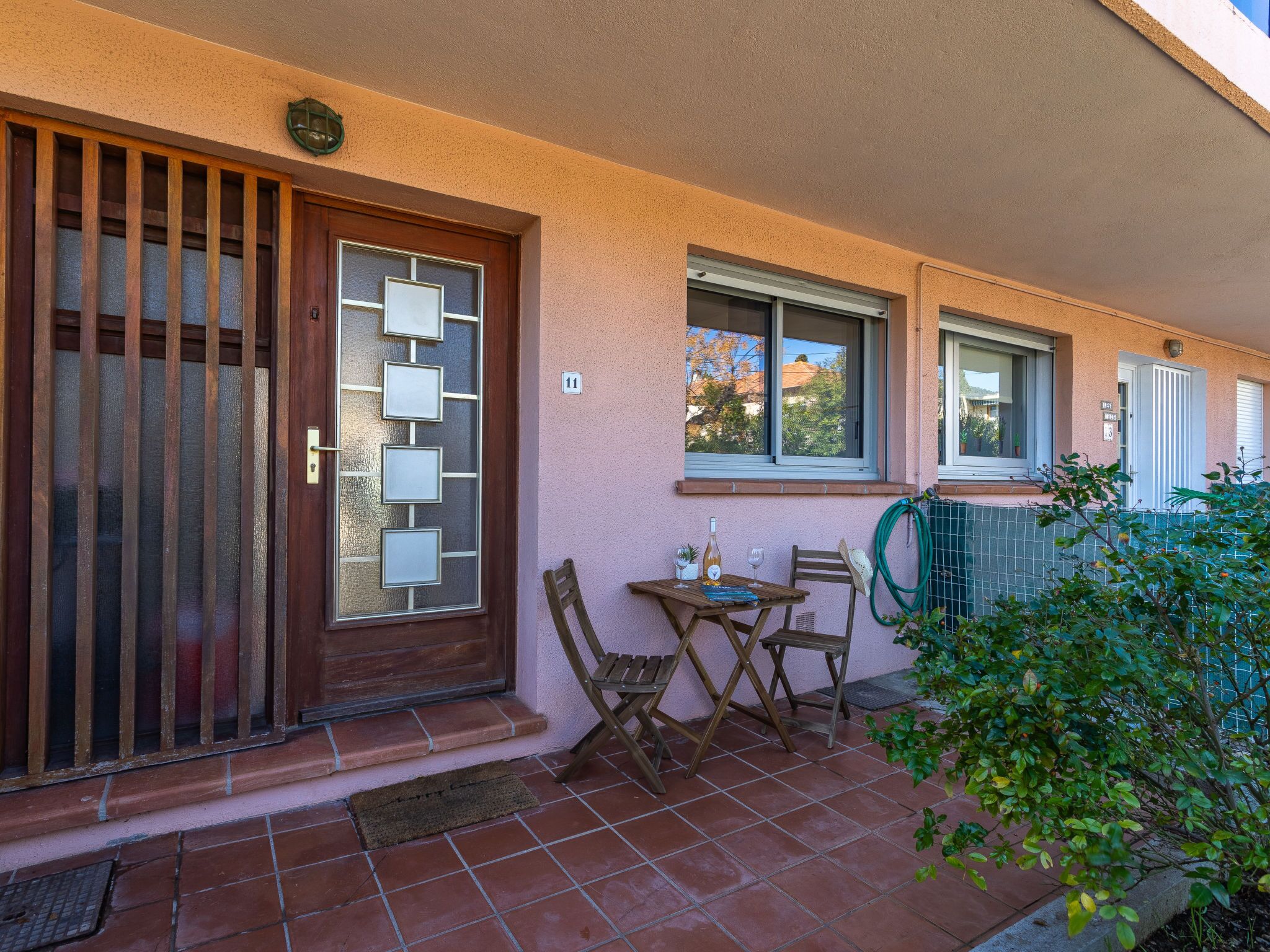 Edificio residencial con puerta de madera, un pequeño patio con mesa y sillas, y una manguera de jardín.