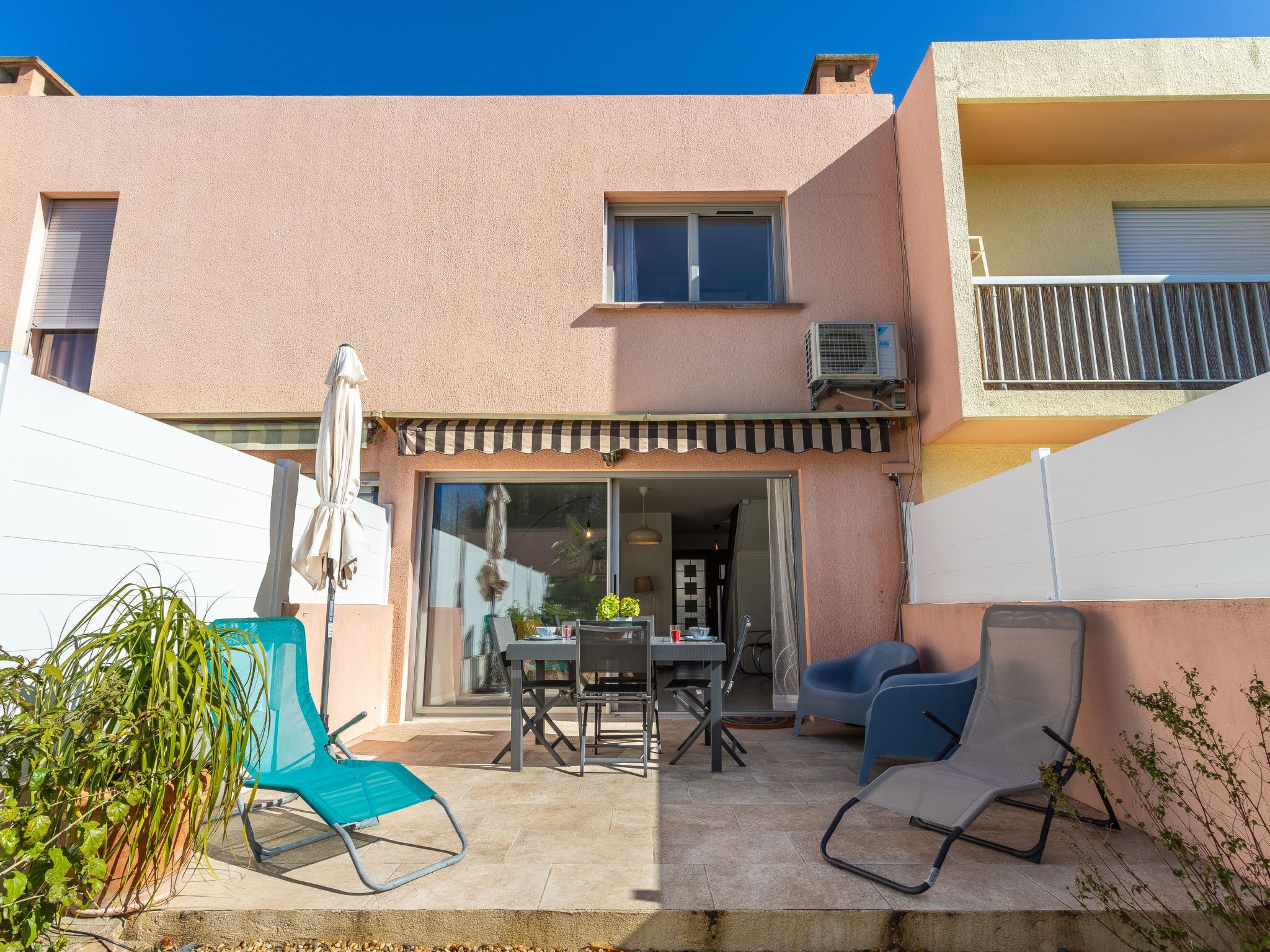 Un bâtiment à deux étages doté d’un patio comprenant une table, des chaises et un parasol.