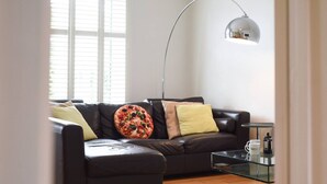 Ein modernes Wohnzimmer mit einem schwarzen Ledersofa, einem Glastisch und einer Stehlampe.