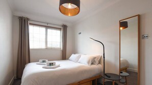 Ein Zimmer mit einem Einzelbett, einem Holzbettgestell, einem Nachttisch, einem Spiegel und einem Fenster mit Vorhängen.