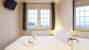 Ein Hotelzimmer mit einem Bett, zwei Fenstern, einem Flachbildfernseher und Blick auf die Stadt.