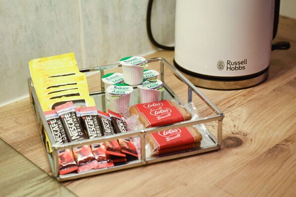 A clear glass display case containing various food items, including Nescafé Original and Lotus Biscuits, on a wooden surface with a white Russell Hobbs kettle in the background. - Superb location 1bedroom apt sleeps 4 w/ Parking! (Old Portsmouth)