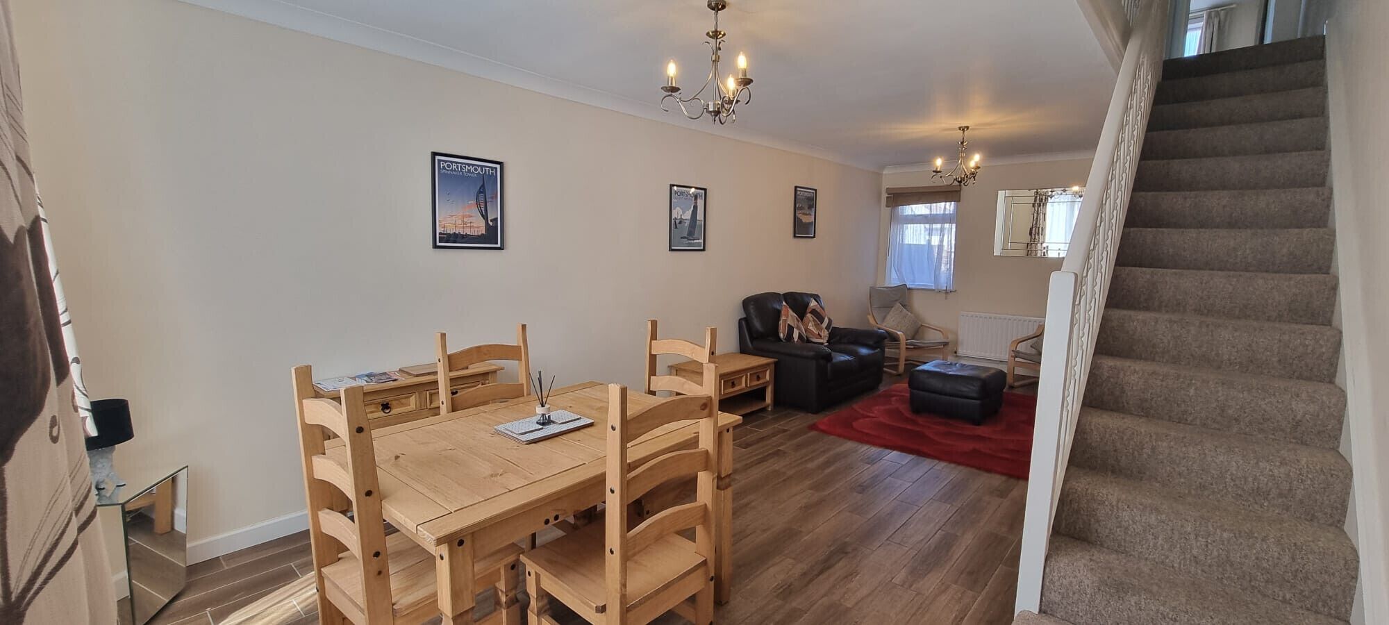 Ein Wohnzimmer mit einem Holzesstisch, zwei Stühlen, einem schwarzen Ledersofa, einem roten Teppich und einer Treppe.