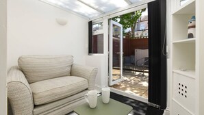 Une pièce comprenant un canapé, une table avec deux tasses blanches et une porte-fenêtre coulissante donnant sur un espace extérieur avec une table et des chaises de patio.