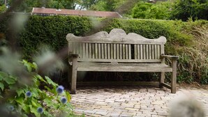 A wooden bench in a garden with a paved pathway and green hedges. - Emsworth`s Cosy Bungalow | Sleeps 3! (West Sussex)