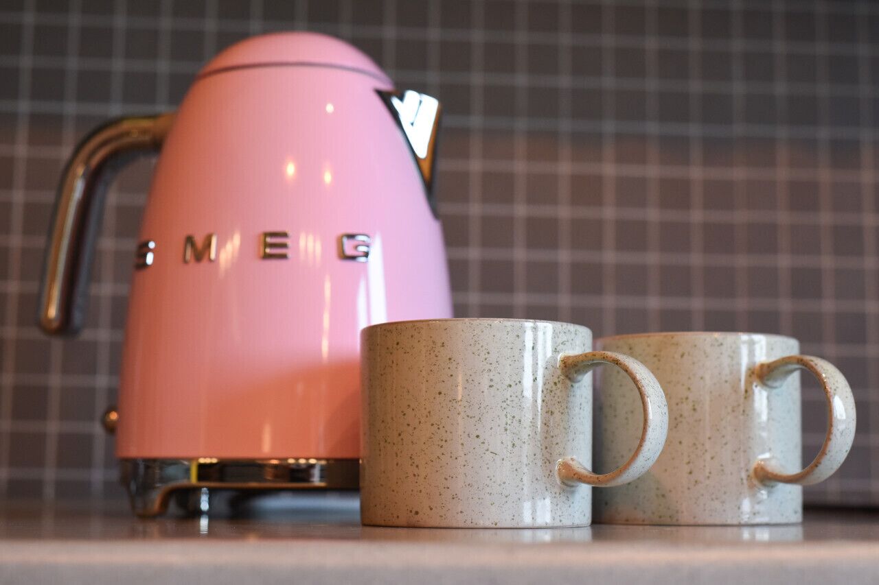 A pink electric kettle and two speckled mugs on a countertop.