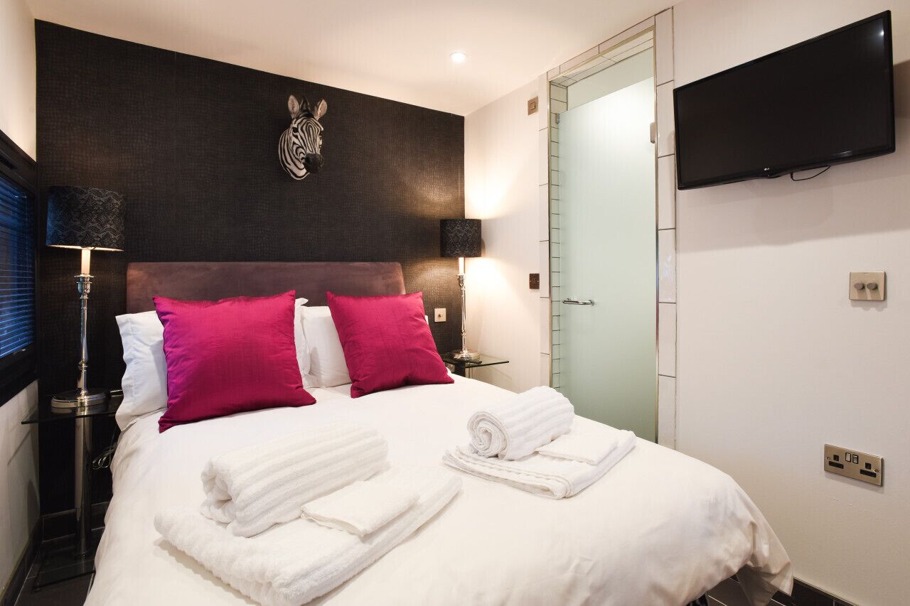 Habitación de hotel con cama, toallas blancas, cabecera de cebra, televisor de pantalla plana y puerta de cristal.