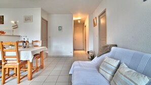 Una habitación limpia y bien iluminada con comedor que incluye una mesa, sillas, un sofá y un pasillo que conduce a otra habitación.