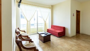 Ein Zimmer mit einem roten Sofa, Holzstühlen, einem kleinen Tisch und einer Schiebetür aus Glas, die auf einen Balkon im Freien führt.