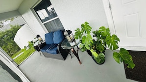 Ein überdachter Patio-Bereich mit Sitzgelegenheit, Topfpflanzen und einer Tür.