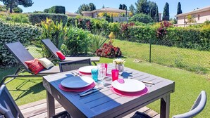 Un patio con tavolo apparecchiato per mangiare, circondato da un giardino curato e affaccio su edifici residenziali.