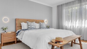 Ein modernes Schlafzimmer mit einem großen Bett, einem Holz-Kopfteil, Nachttischen und einer Bank mit Hut und Sonnenbrille.