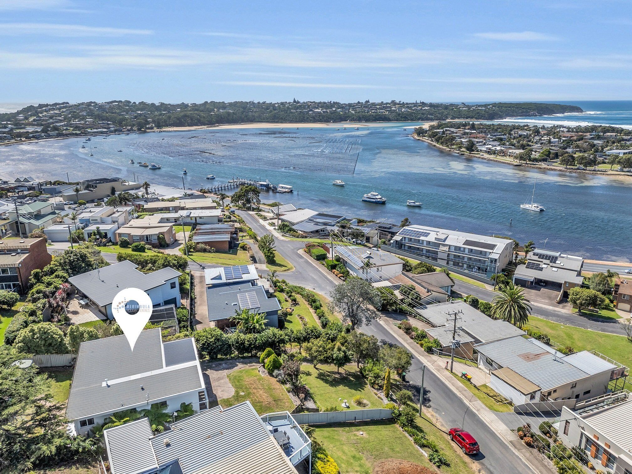 Vue aérienne d’un quartier résidentiel situé sur la côte, avec des maisons modernes, une marina remplie de bateaux et une vue dégagée sur l’océan.