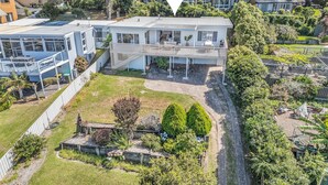 Ein modernes, zweistöckiges Gebäude mit überdachter Außenbereich-Sitzgruppe, umgeben von üppiger Vegetation und einem gepflegten Garten.