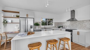 Une cuisine moderne dotée d’un îlot central, de tabourets en bois et d’appareils électroménagers intégrés.