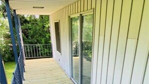 Una terraza de madera con barandilla metálica, puertas correderas de vidrio y pared exterior blanca.