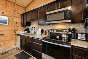 A modern kitchen with dark wooden cabinets, stainless steel appliances, and a granite countertop.