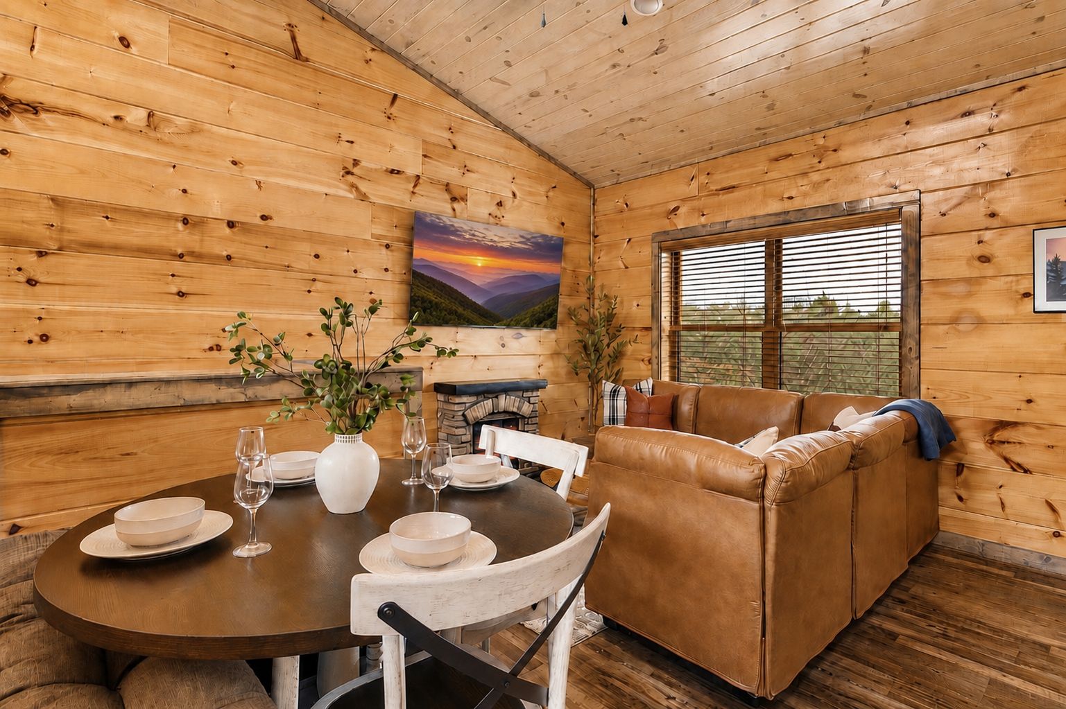 A wooden interior with a round table set for dining, a leather sofa, and a fireplace.