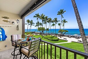 Een balkon met uitzicht op de oceaan, palmbomen en een verzorgd zitgedeelte buiten.