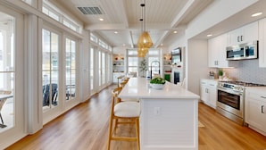 Una cocina amplia con una isla central, taburetes de madera y una lámpara colgante.