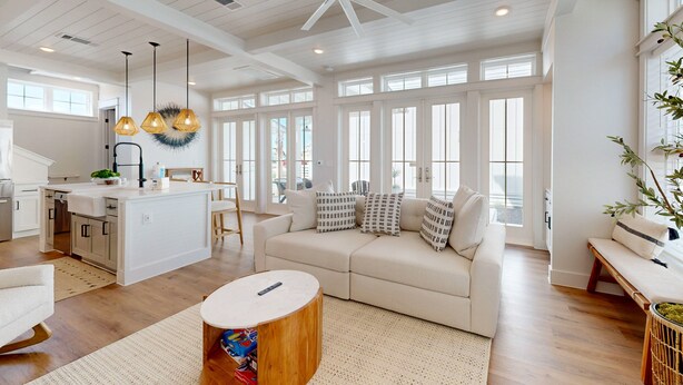 Un espacio habitable amplio con un gran ventanal, un sofá blanco, una mesa de centro de madera y una cocina con una isla blanca.