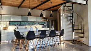 Una cocina moderna con una isla central, sillas negras y una escalera espiral.