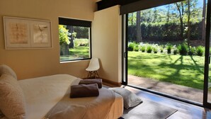 Un dormitorio con una cama grande, una silla y vistas a un jardín a través de una puerta corrediza de vidrio.