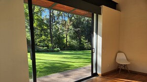 Una habitación con un amplio ventanal corredera que da a un césped y árboles bien cuidados.