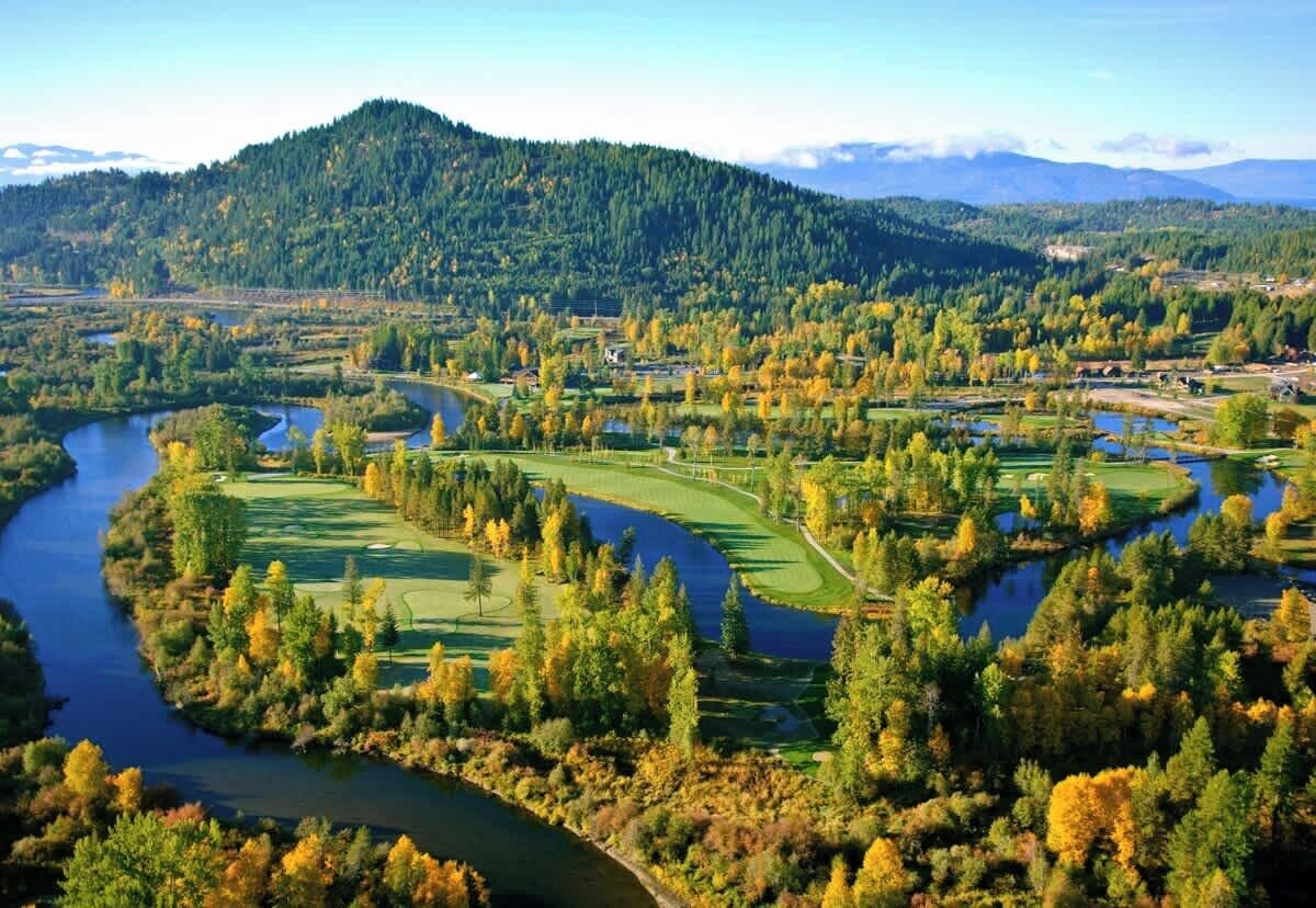 Un parcours de golf traversé par une rivière, entouré de collines boisées.