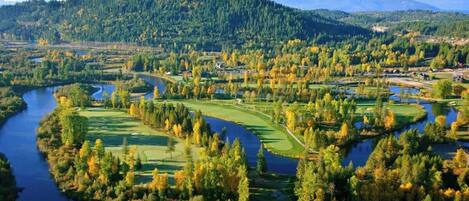 Un parcours de golf traversé par une rivière, entouré de collines boisées.