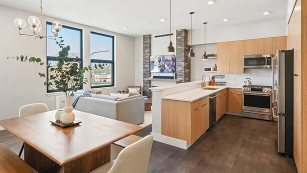 A modern kitchen with wooden cabinets, stainless steel appliances, and a dining area with a table and chairs.