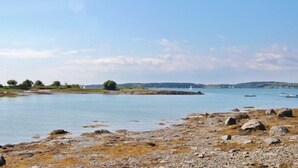 A rocky shoreline with calm water, boats, and distant trees.