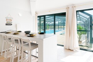 A modern kitchen with a dining area, large windows, and a view of a swimming pool. - GuestReady - Quinta do Sol (Mealhada)