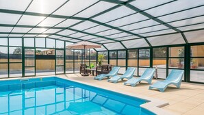 Una piscina con sillas de descanso y una mesa bajo una estructura de techo de vidrio.