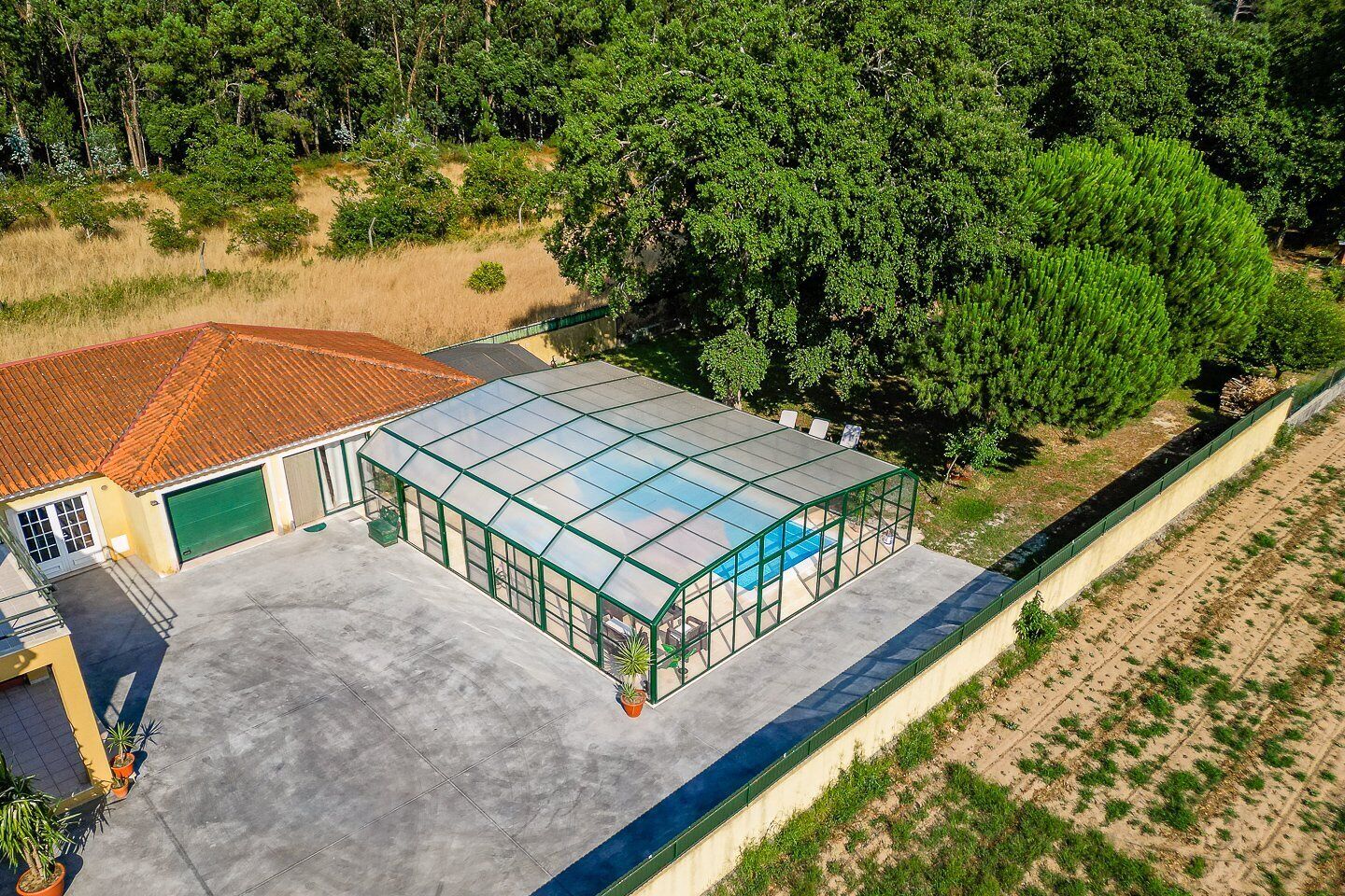 A greenhouse with a glass roof, adjacent to a building with a red-tiled roof and a green garage door.