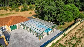 A greenhouse with a glass roof, adjacent to a building with a red-tiled roof and a green garage door.