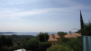 A coastal view with a house featuring a tiled roof, surrounded by greenery and overlooking the sea.