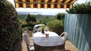 An outdoor patio with a table and chairs, surrounded by greenery and a view of the landscape.