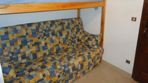 A small, cozy room with a wooden headboard above a sofa covered in a checkered fabric.