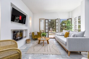 A modern living room with a flat-screen TV, a sofa, a coffee table, and a wicker chair.