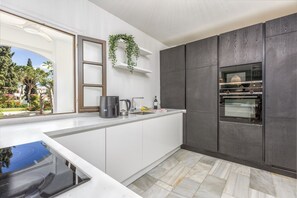 Une cuisine moderne dotée d’un four encastré, de meubles blancs et d’une fenêtre donnant sur un jardin.