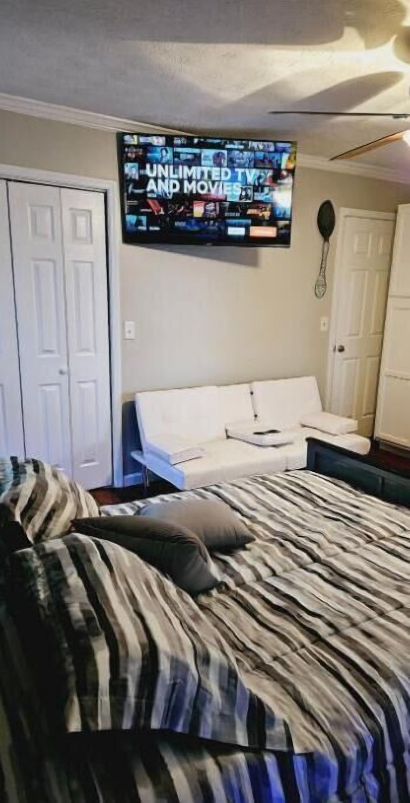 A bedroom with a bed, a white couch, a flat-screen TV on the wall, and a door.