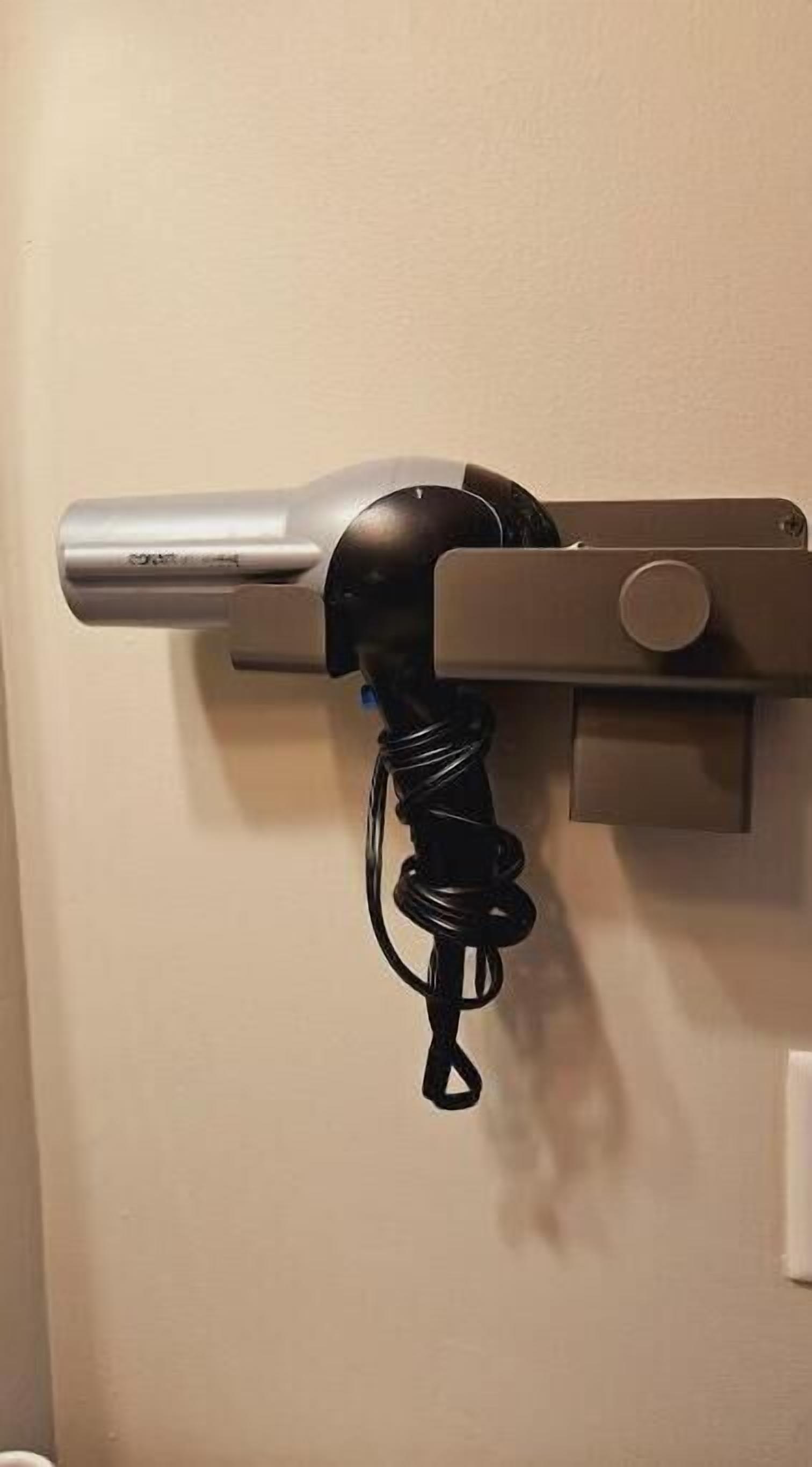 A hairdryer mounted on a wall with a coiled cord.