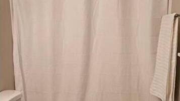 A bathroom with a white shower curtain, a white toilet, and a white bath mat.