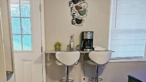 A small kitchen with two white bar stools, a coffee maker, and a decorative wall piece. - Studio Kevdaya 1 (Norcross)
