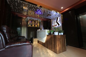 Zona de recepción con un mostrador de madera, un sofá de cuero y una pared decorativa con un logotipo.