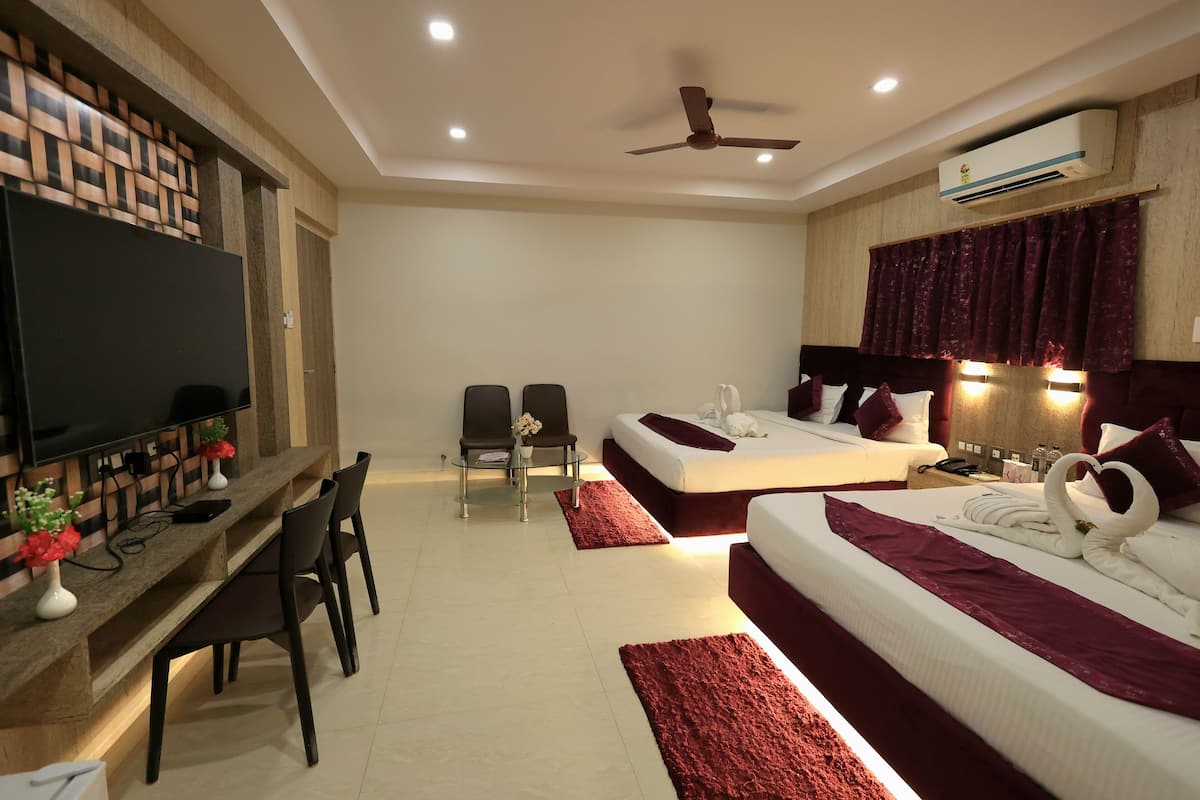 Une chambre d’hôtel moderne équipée d’une télévision à écran plat, d’un bureau avec des chaises, de deux lits avec une literie rouge, d’un ventilateur de plafond et d’un appareil de climatisation.
